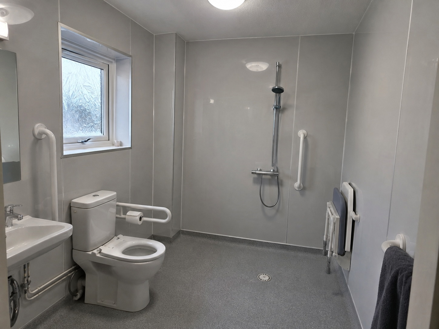 Grey hygienic PVC wall cladding and coved safety vinyl flooring in an accessible wet room with level-access shower in Bridgwater, Somerset